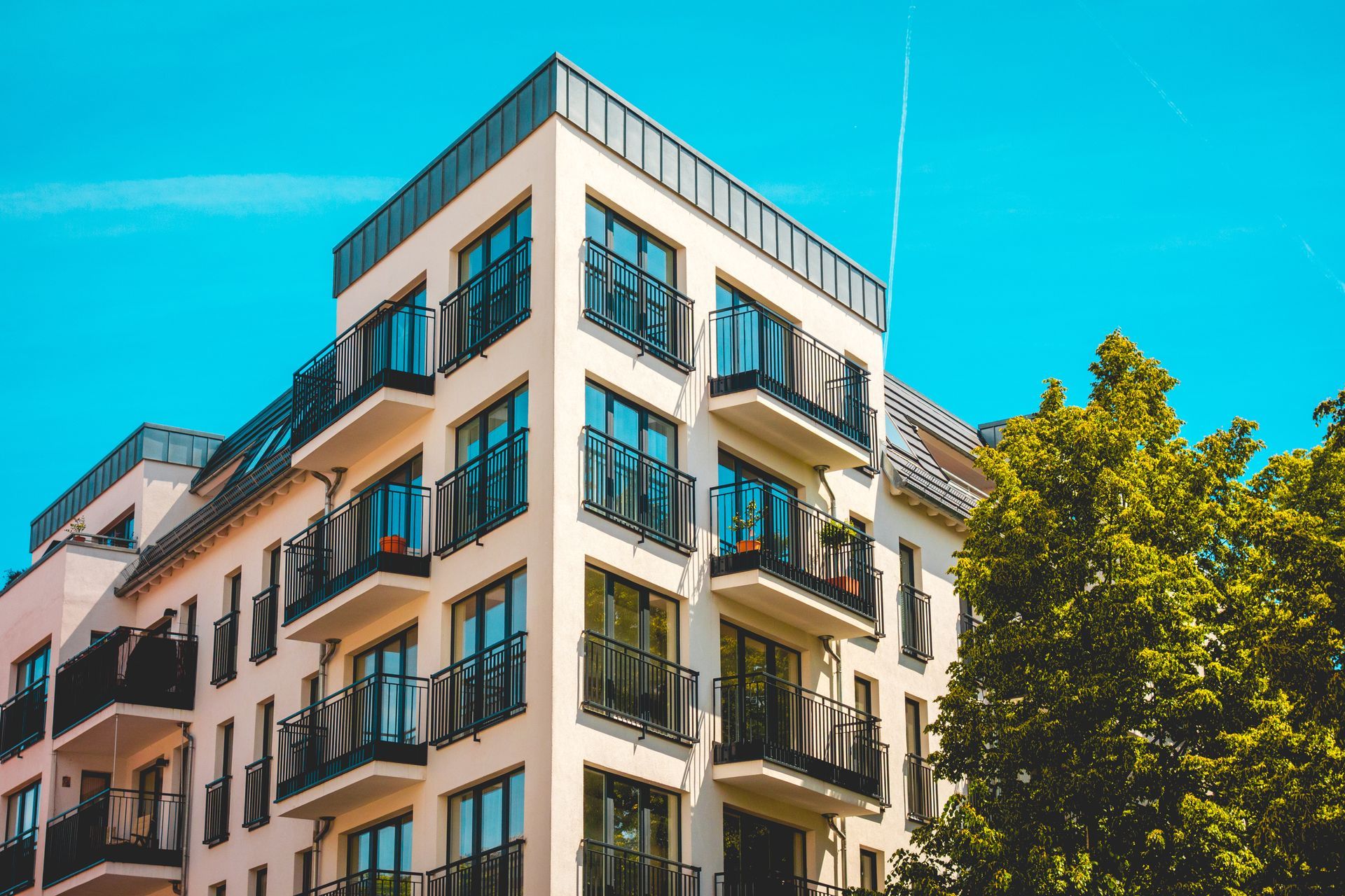 Modern, cream-colored apartment building with black balconies against a clear blue sky and lush green tree. Modern, cream-colored apartment building with black balconies against a clear blue sky and lush green tree.