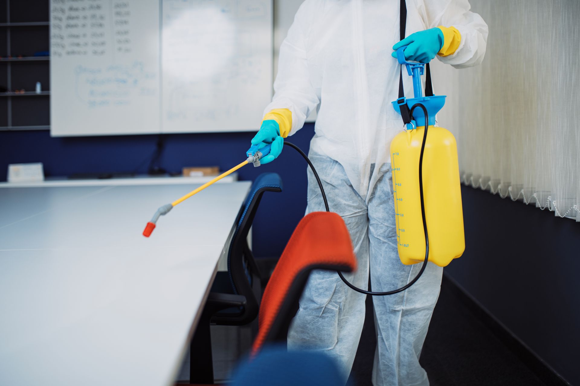 Person in protective suit spraying a desk with a yellow tank sprayer. Person in protective suit spraying a desk with a yellow tank sprayer.