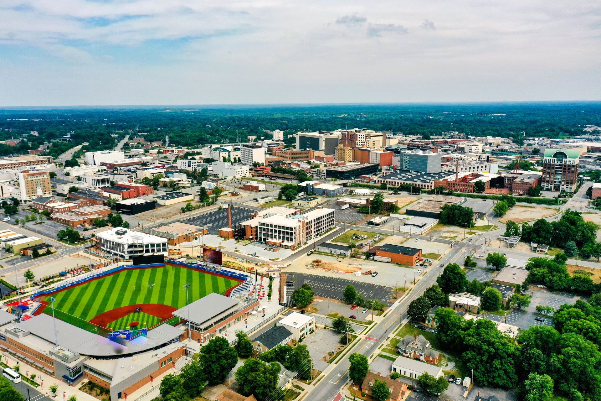 Aerial view of a city with a baseball field in the foreground; several buildings and green trees are visible. Aerial view of a city with a baseball field in the foreground; several buildings and green trees are visible.