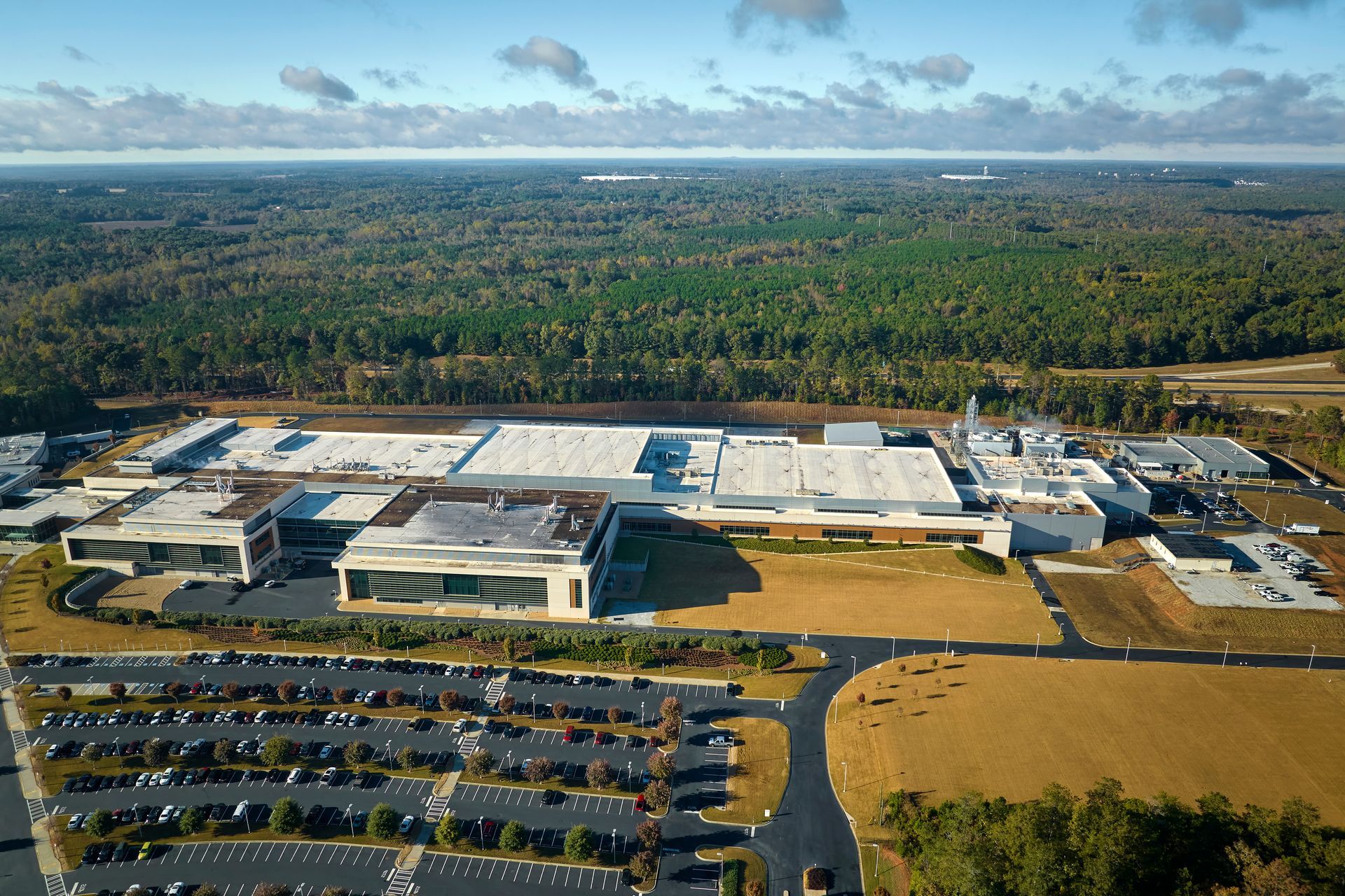 Aerial view of a large industrial complex with several buildings, surrounded by parking lots and a forest. Aerial view of a large industrial complex with several buildings, surrounded by parking lots and a forest.