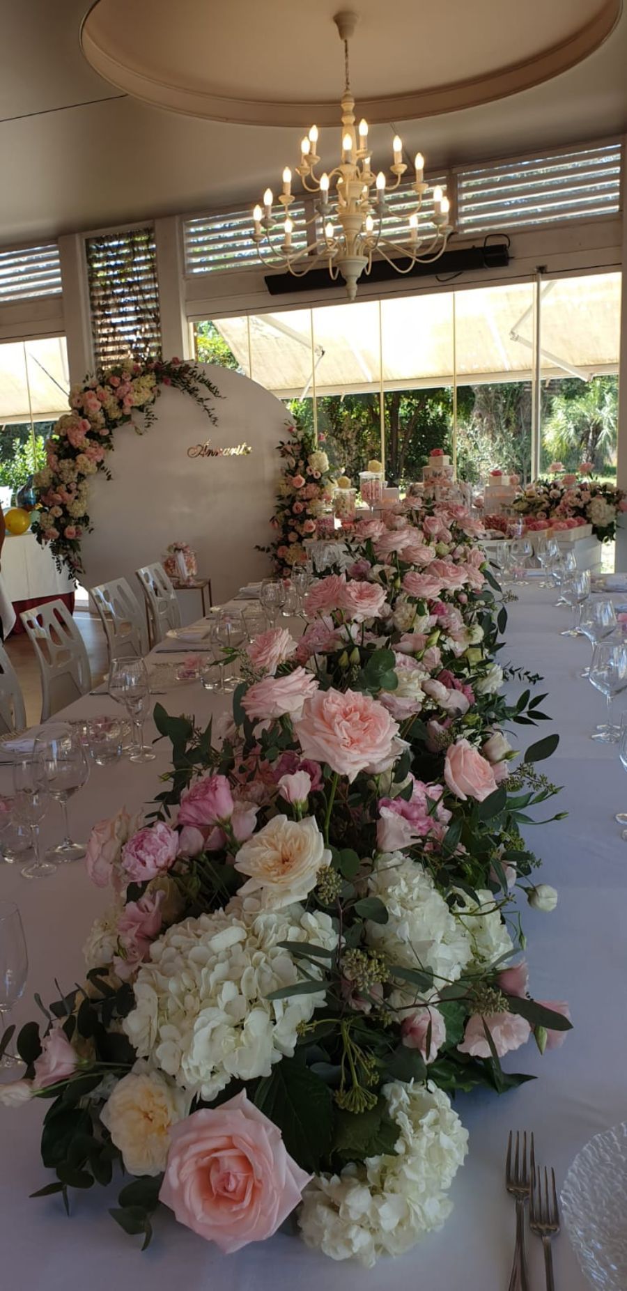 tavolo lungo allestito con fiori rosa e bianchi