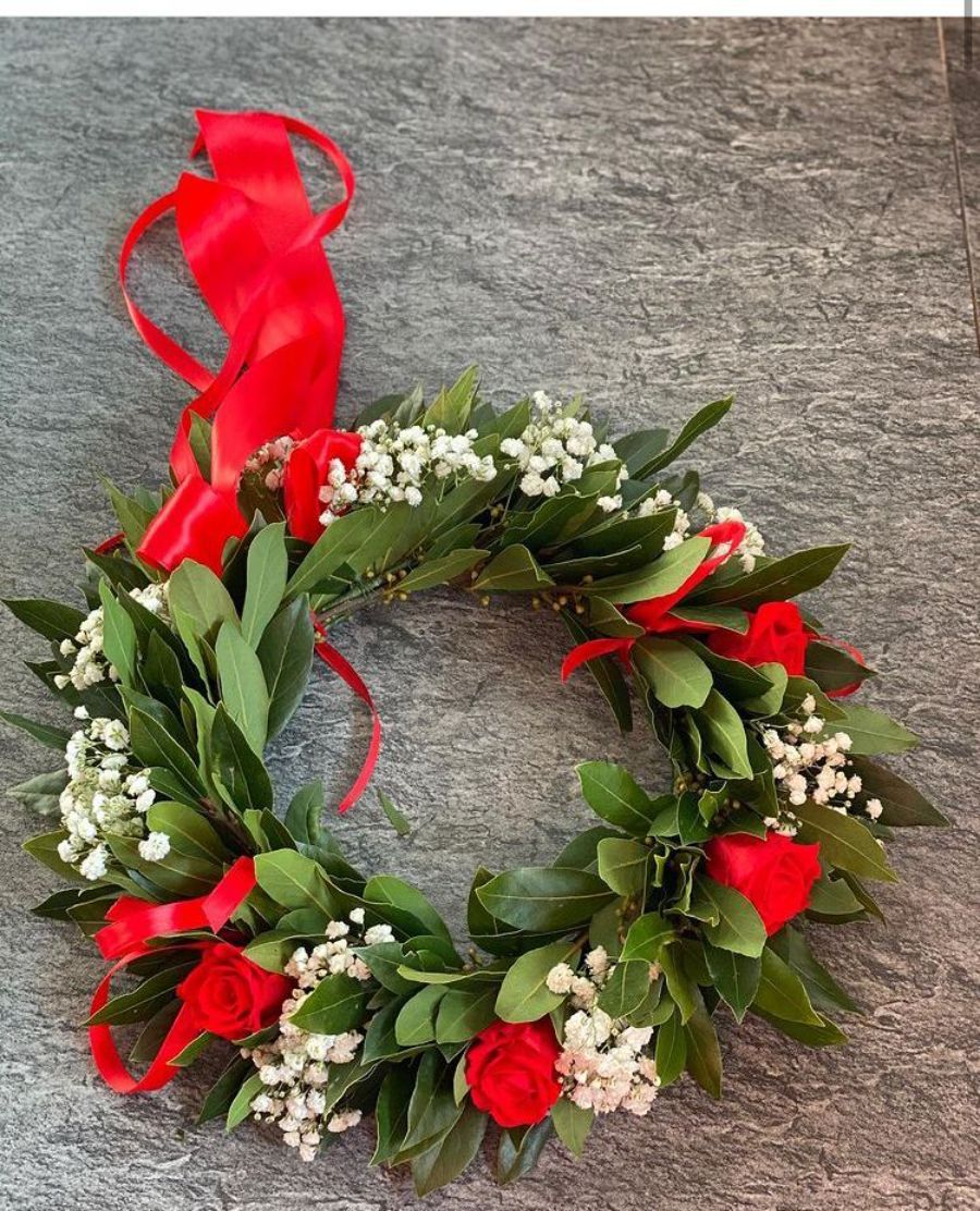 corona d'alloro con rose rosse, fiori bianchi e nastro rosso
