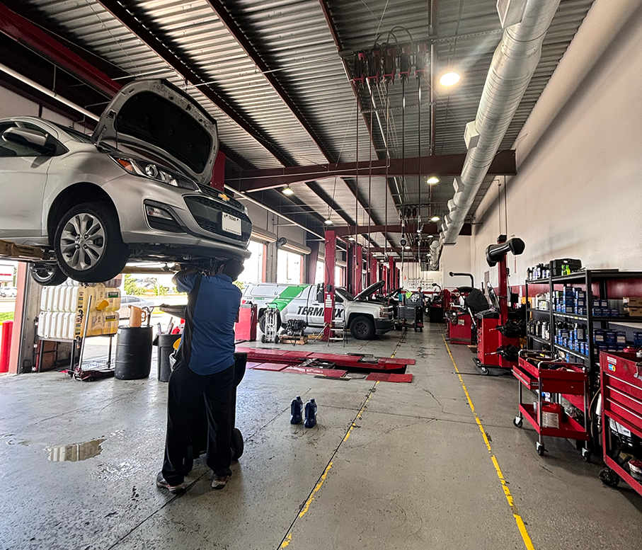 A man is lifting a car in a garage with the hood open. | Elite Auto Experts