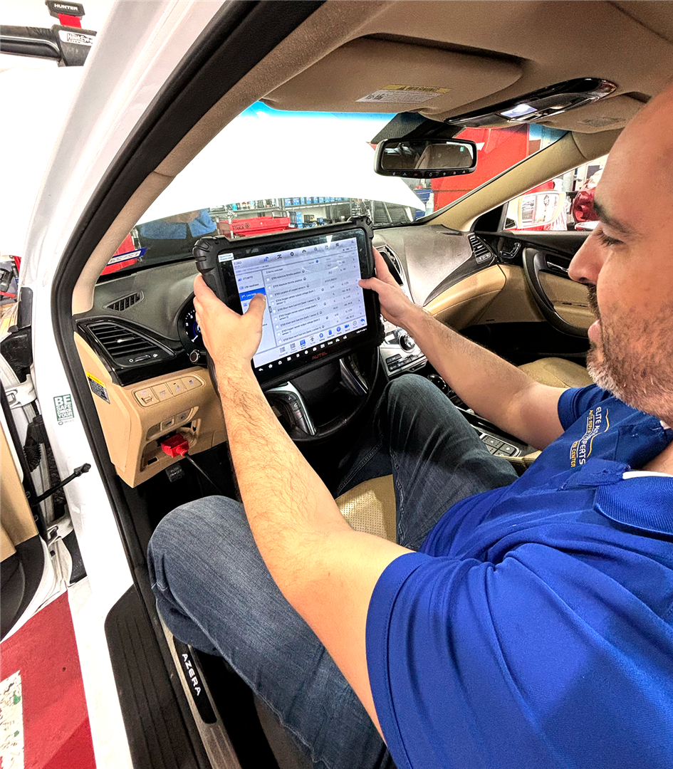 A man in a blue shirt is sitting in a car using a tablet. | Elite Auto Experts