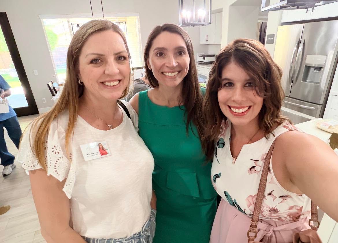 Three women smiling in a bright kitchen, posing for a selfie.