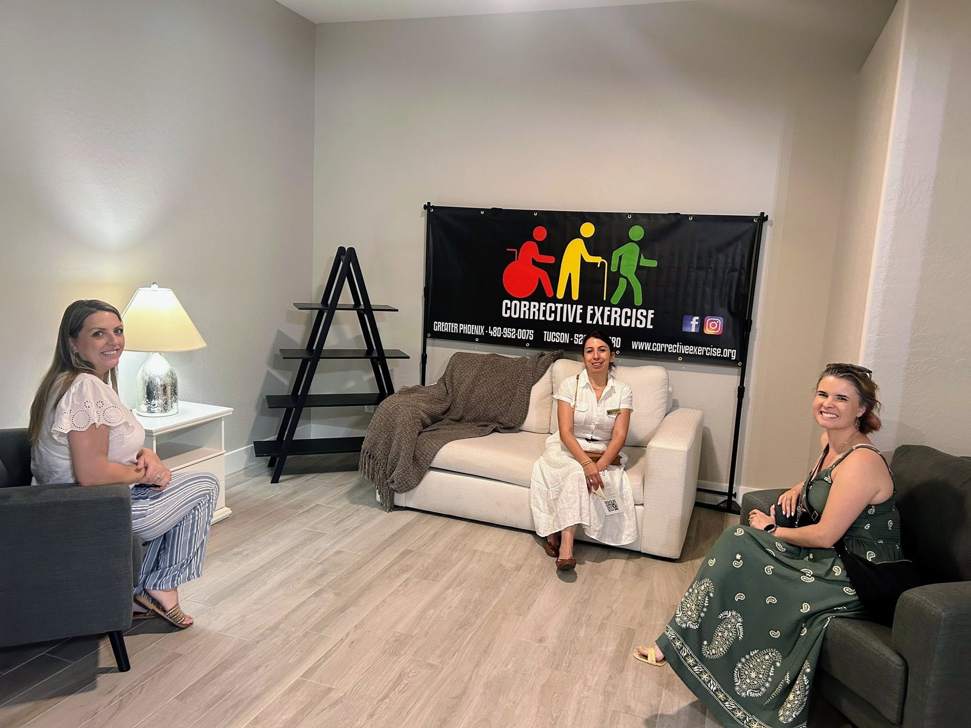 Three people sit in a living room with a black banner on the wall and decorative seating.