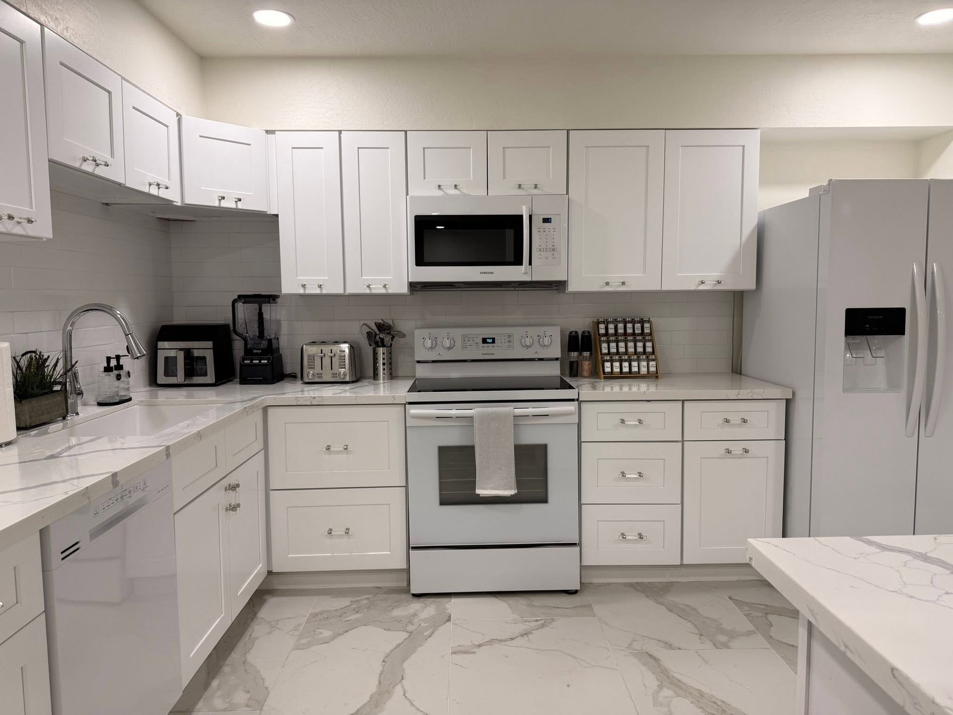 Bright white kitchen with cabinets, stove, microwave, dishwasher, and refrigerator.
