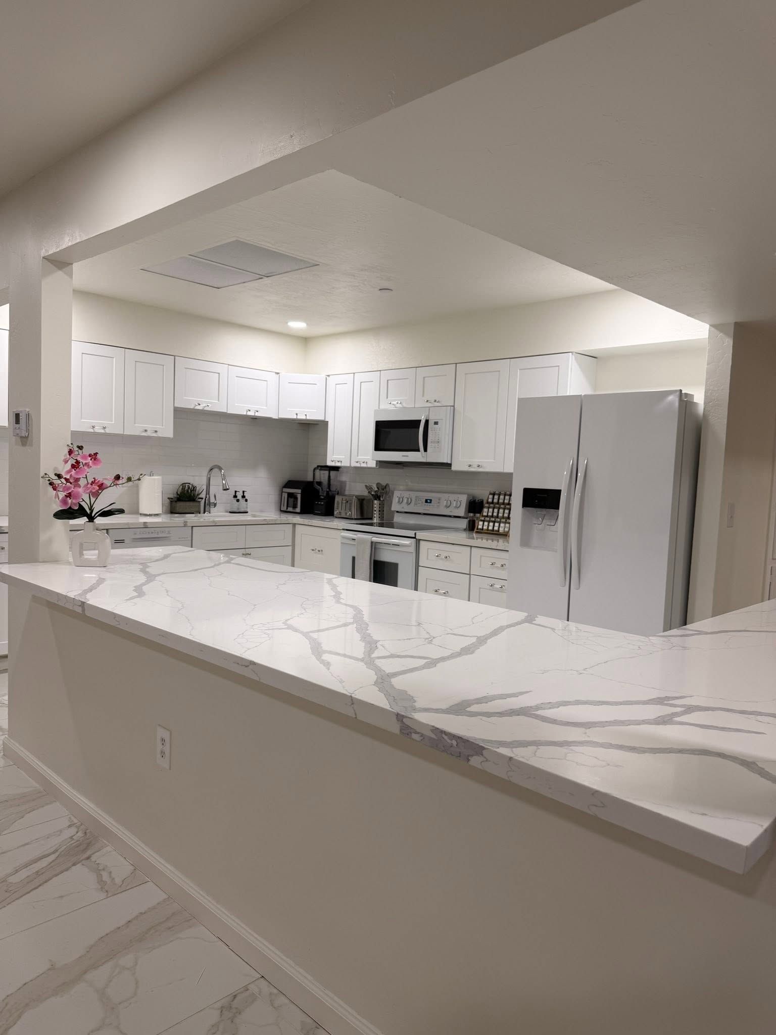Bright white modern kitchen with marble island, white cabinets, stainless appliances, and recessed lighting