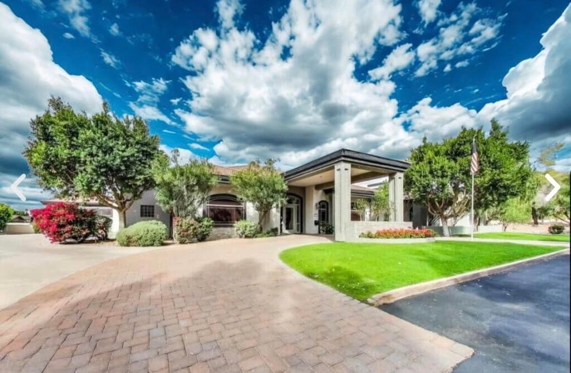 Suburban house with stone driveway, green lawn, palm trees, and bright blue sky with clouds