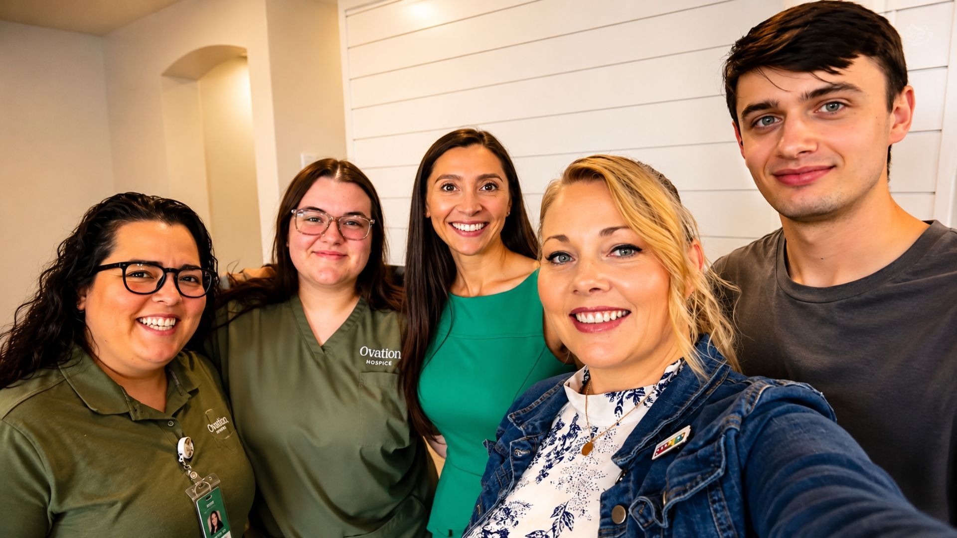 Five coworkers smiling for a selfie in a bright office hallway.