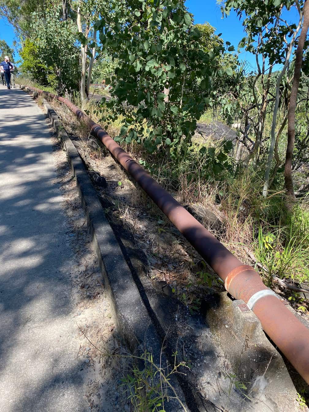 A person is walking down a path next to a large pipe.