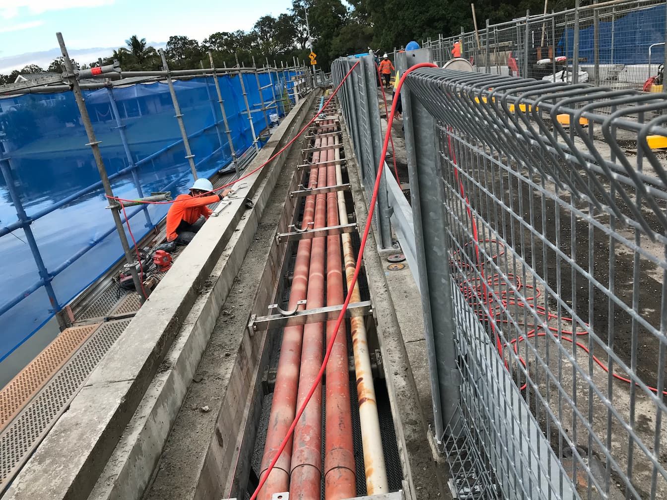 A bunch of pipes are being installed in a trench next to a fence.