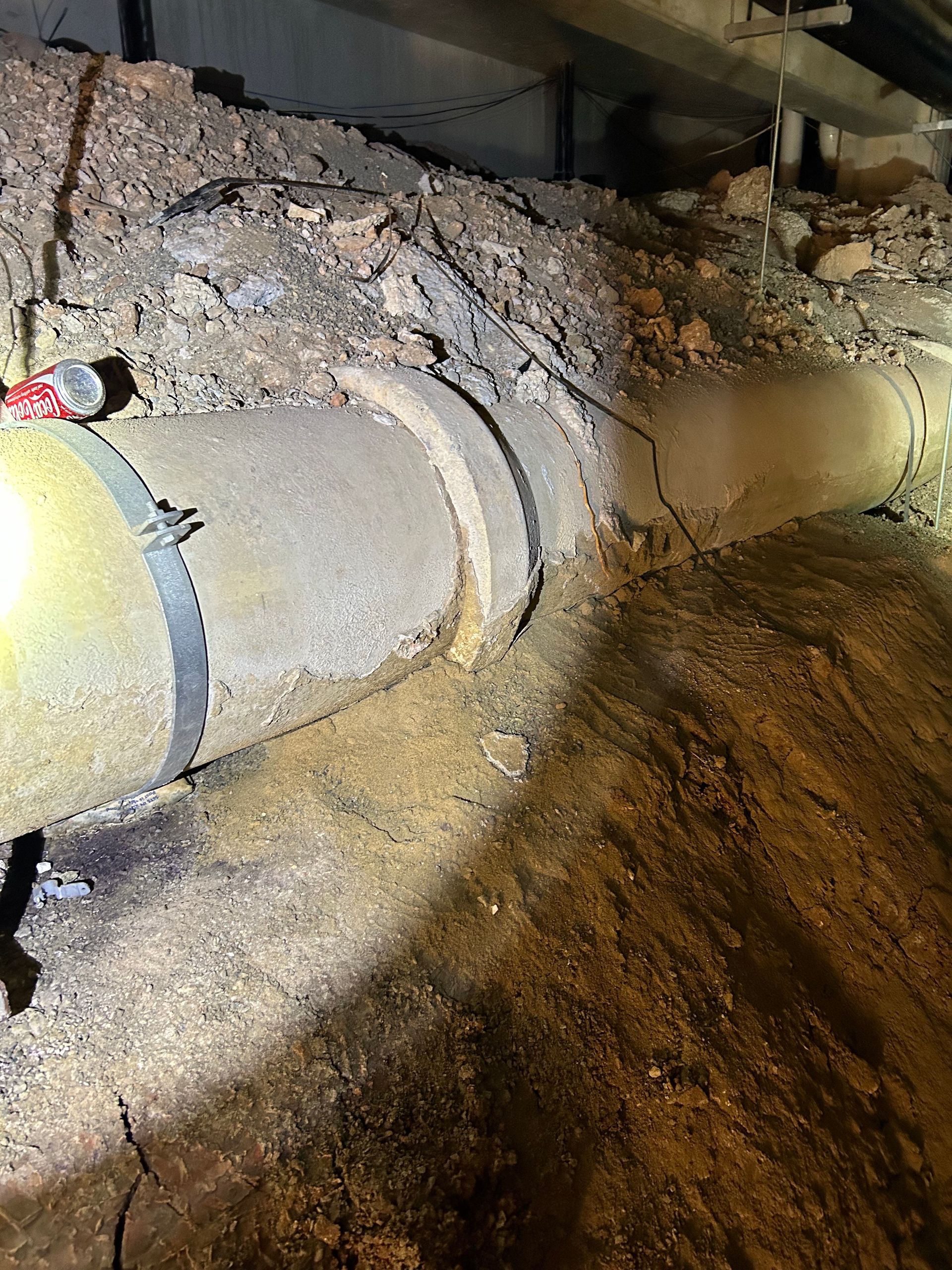 A large pipe is sitting in the dirt under a house.