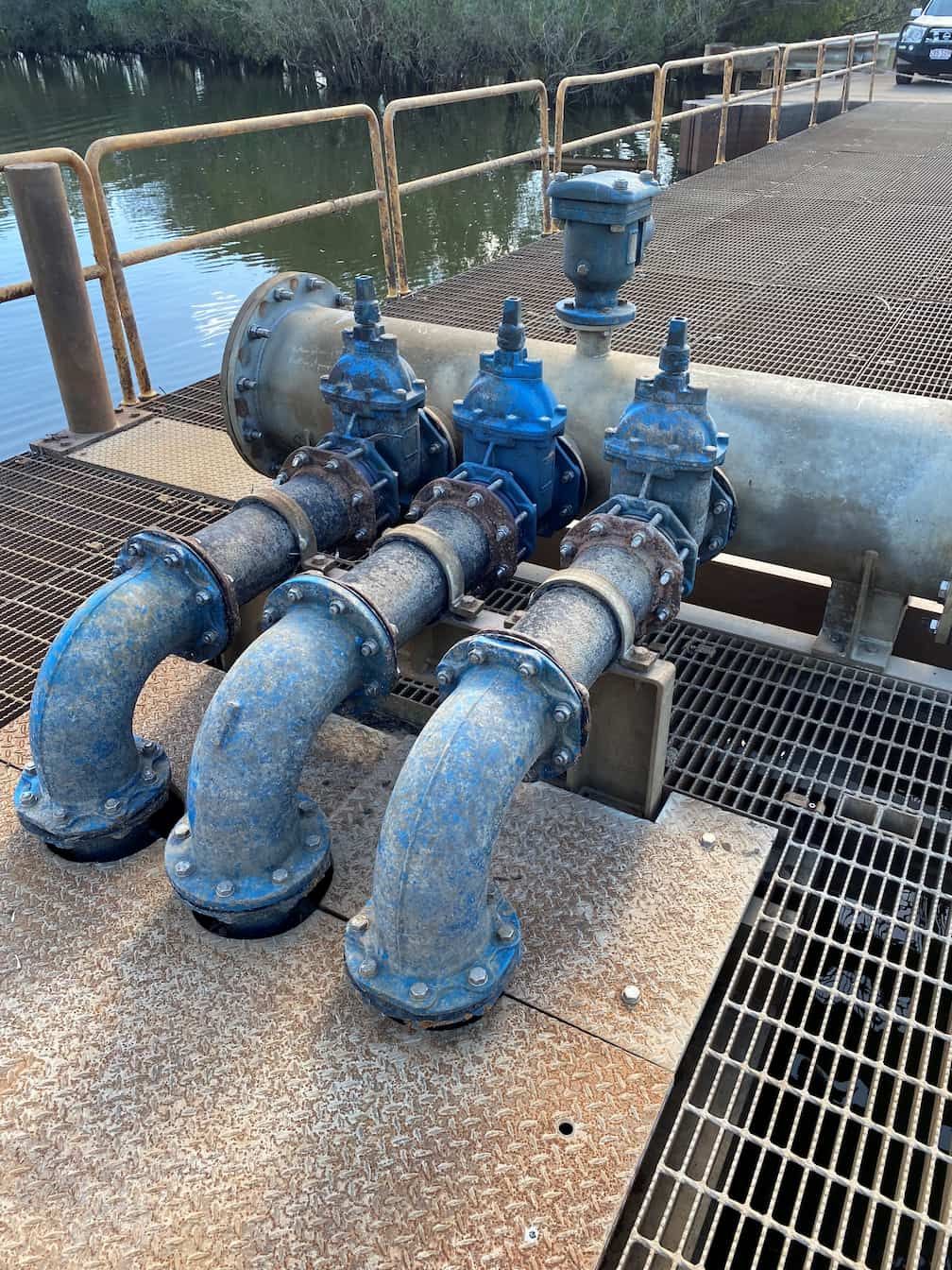 A bunch of pipes are sitting on top of a metal grate next to a body of water.