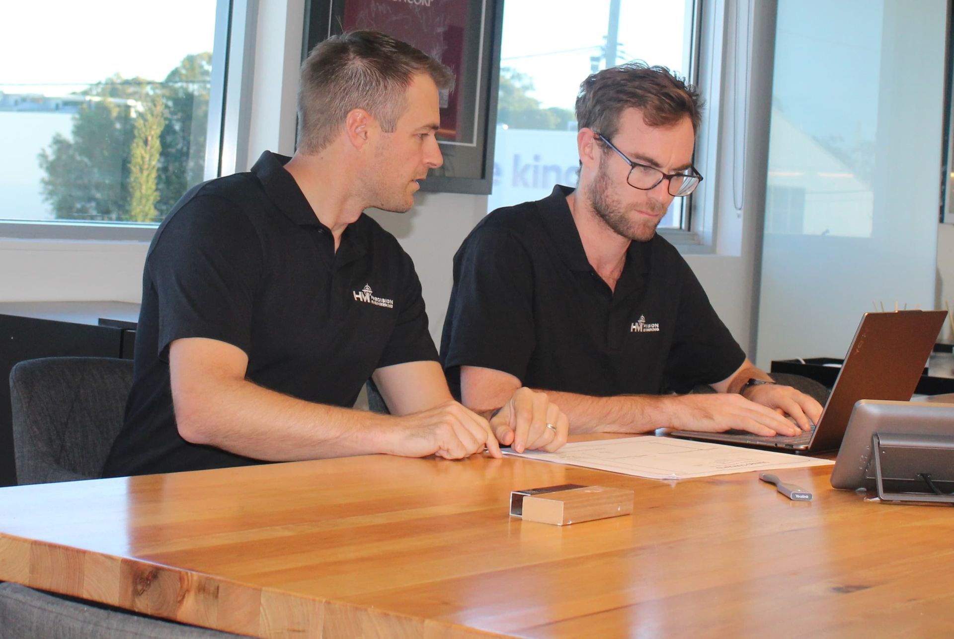 Two men are sitting at a table looking at a laptop.