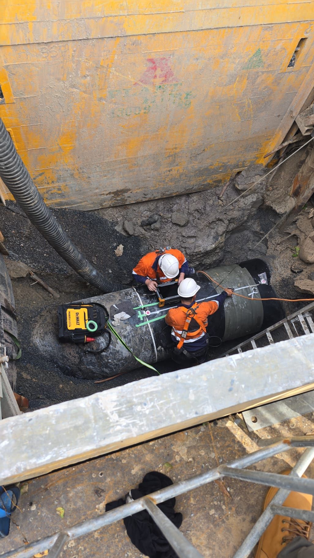 Two men are working on a pipe in a hole.