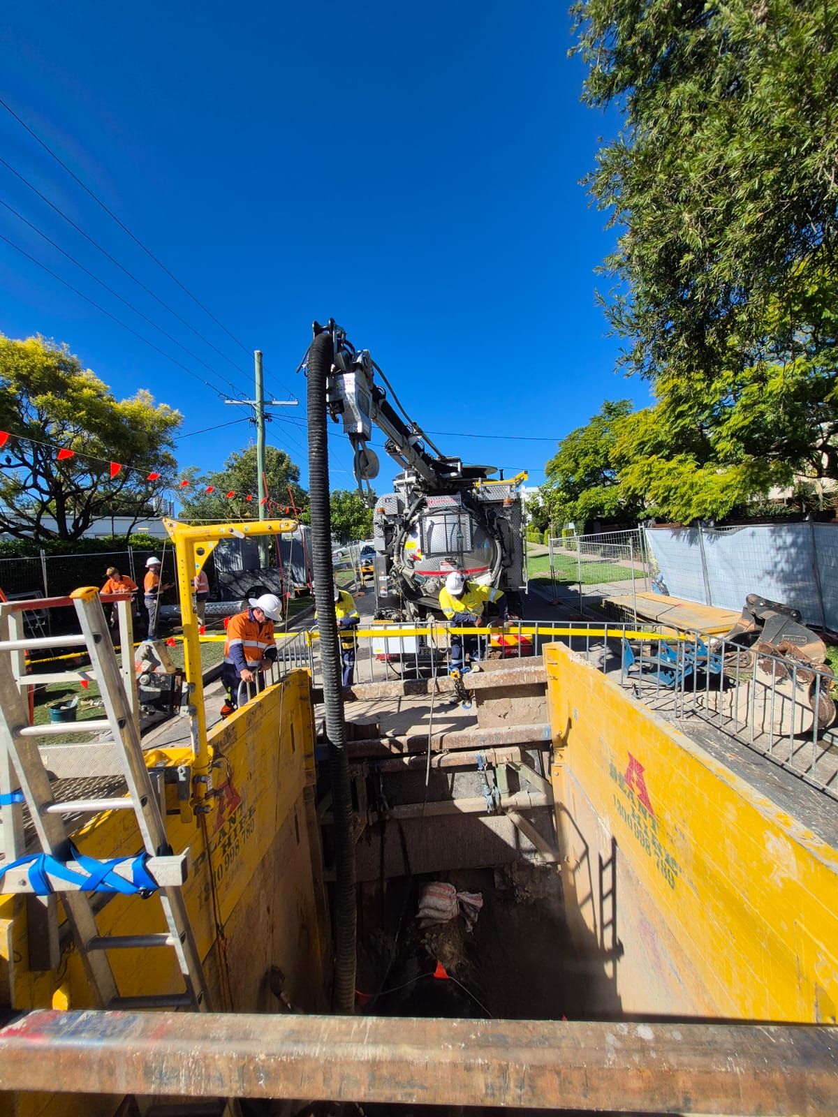 A bunch of pipes are being installed in a trench next to a fence.