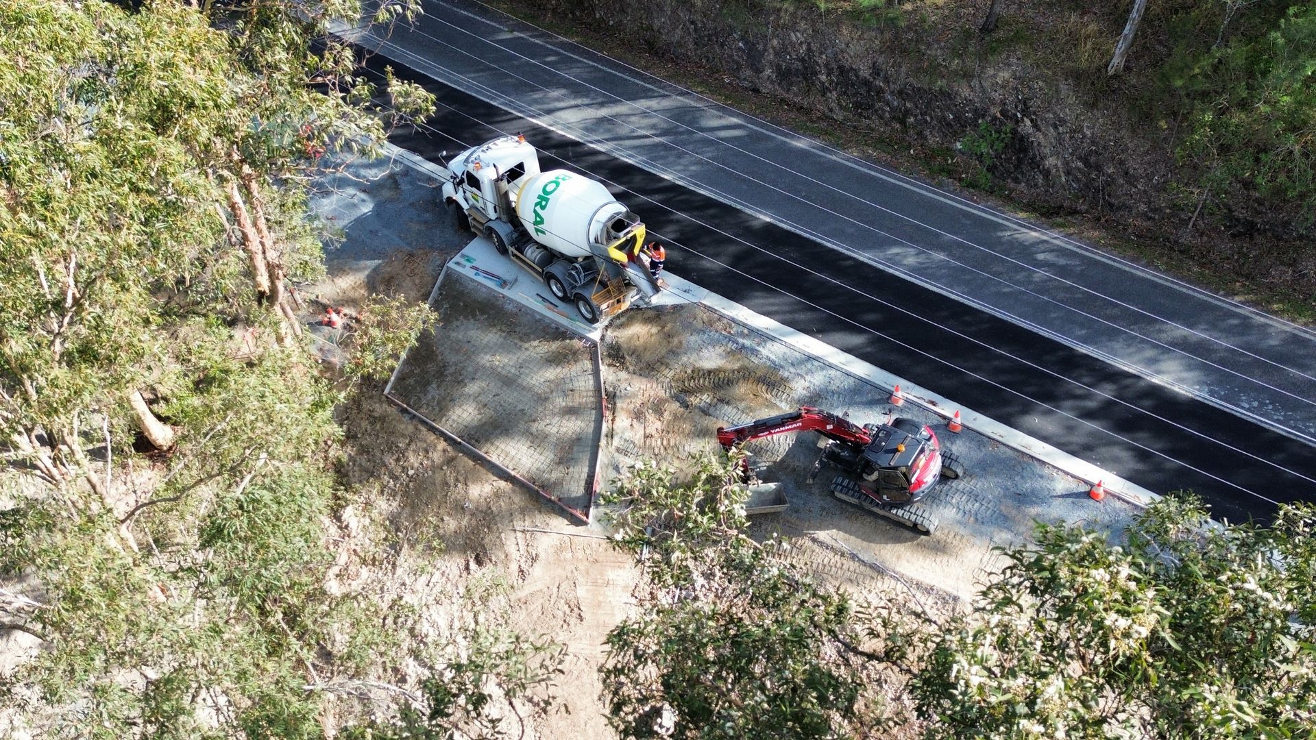 A cement truck pouring concrete onto a road construction site next to an excavator.
