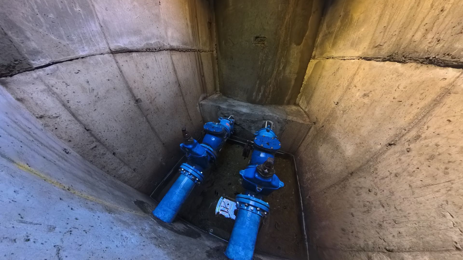 Blue pipes and valves inside a concrete utility pit, viewed from above.