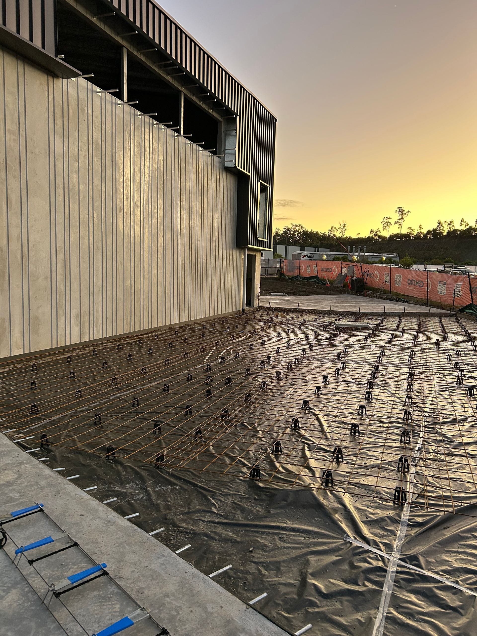 Construction site with rebar grid prepared for concrete, building facade, sky at dusk.