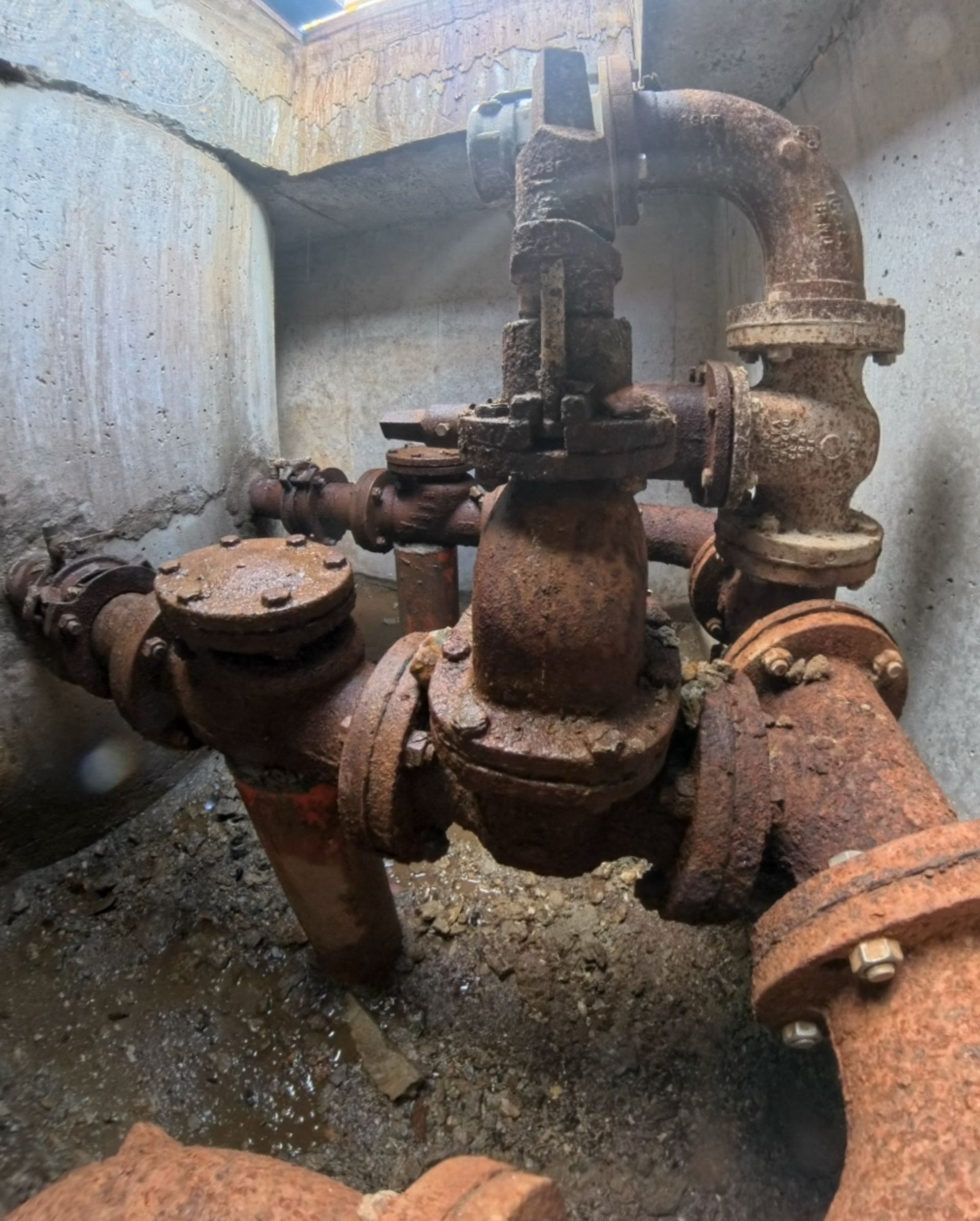 Rusty sewer pipes and valves in a concrete pit