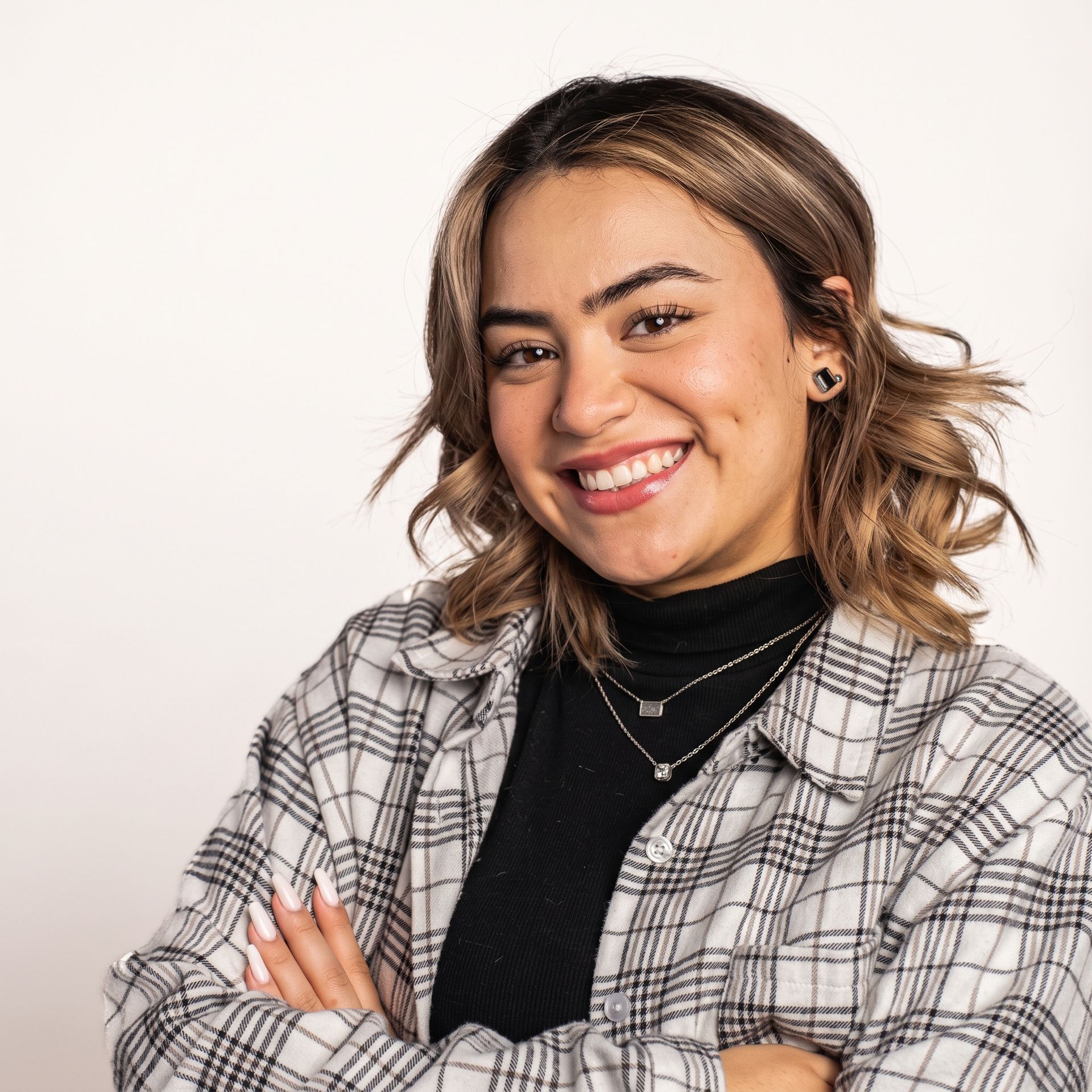 Smiling woman in a plaid shirt and black turtleneck with arms crossed against a light background
