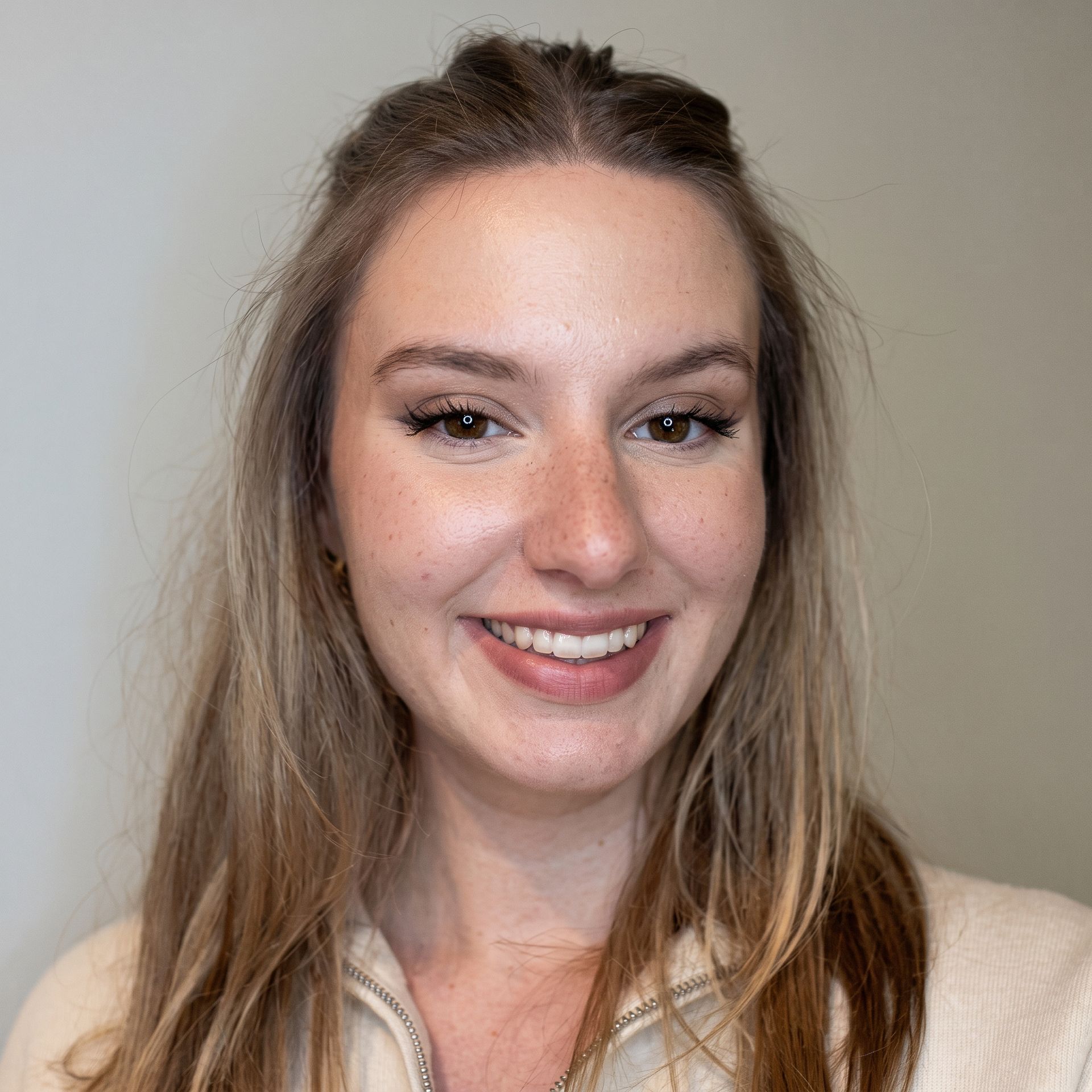 Smiling woman with long brown hair against a plain gray background
