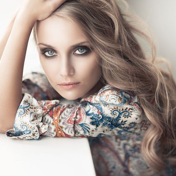 Portrait of a woman with long wavy hair, resting on her arm in a patterned top, gazing at the camera