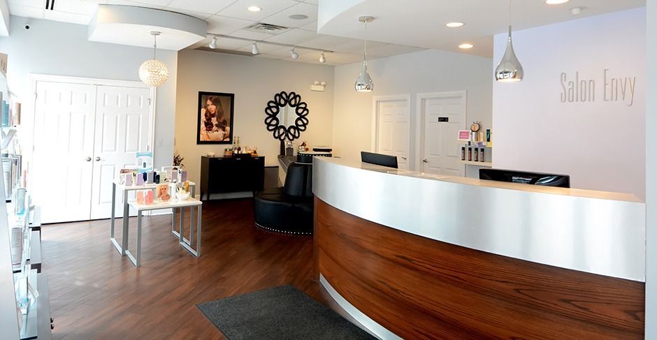 Bright lobby with curved wooden reception desk, black seating, and white walls under recessed lighting