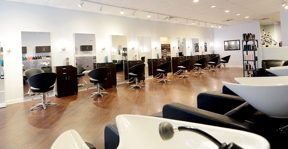 Modern hair salon with styling chairs, mirrors, wash basins, and bright wood floors