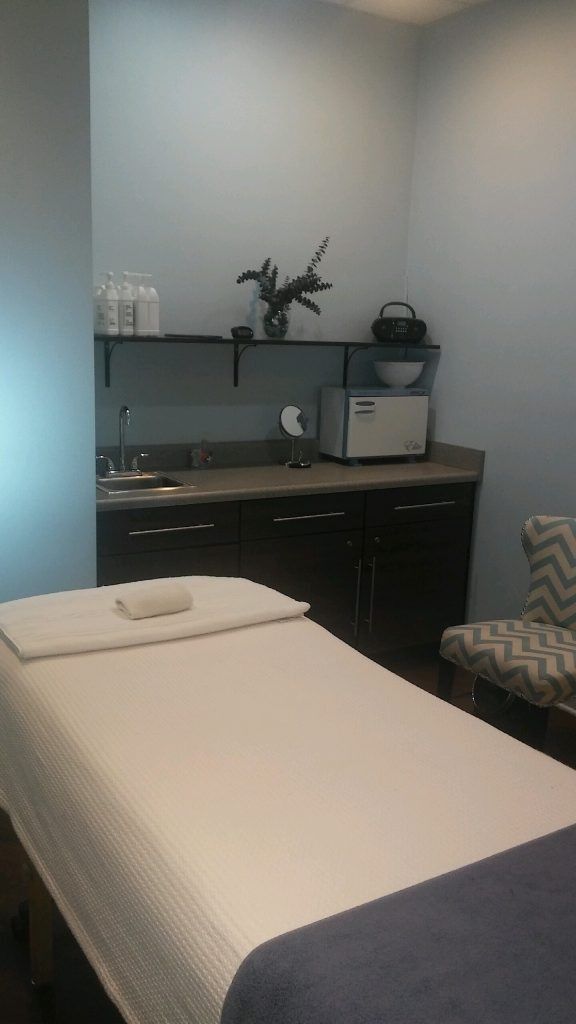 Small treatment room with a massage table, shelves, and medical equipment on dark cabinets.