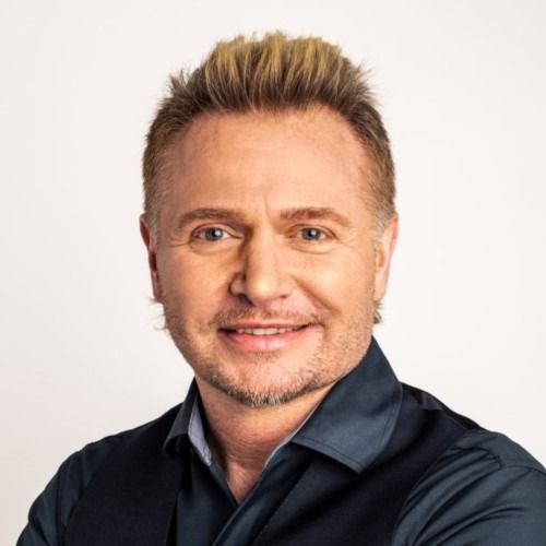 Portrait of a smiling man in a dark shirt against a light background
