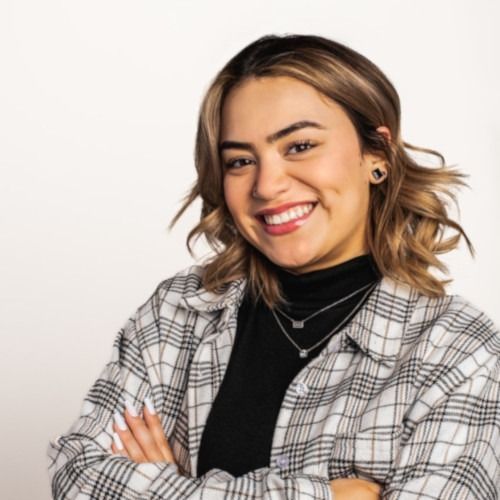 Smiling person in a plaid shirt and black turtleneck with arms crossed against a white background