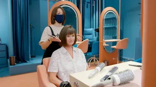 Woman getting a haircut at a salon, with a stylist behind her and blue walls in the background