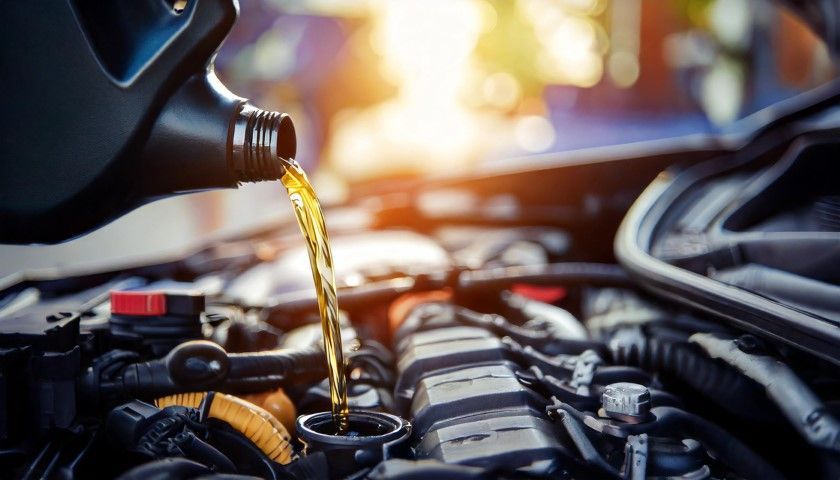 Motor oil being poured into a car engine bay, with warm sunlight in the background.