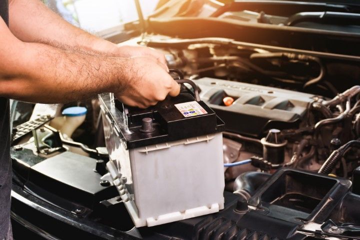 Hands placing a car battery into an engine bay under an open hood.