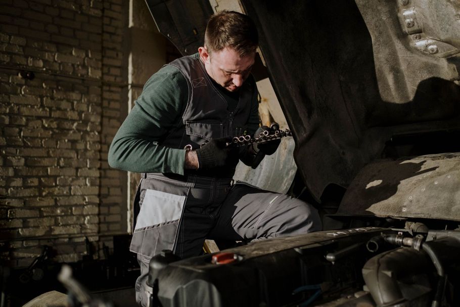 Man kneeling in a dark workshop, inspecting a small object beside an open metal case