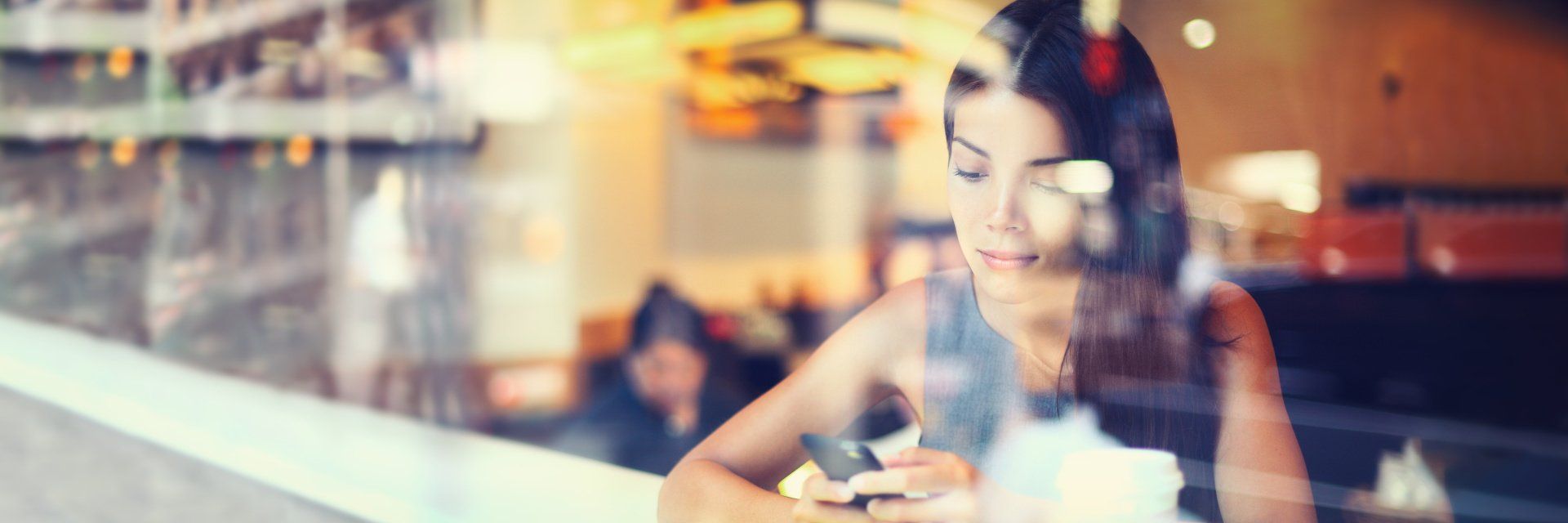 Eine Frau sitzt an einem Tisch in einem Restaurant und schaut auf ihr Telefon.