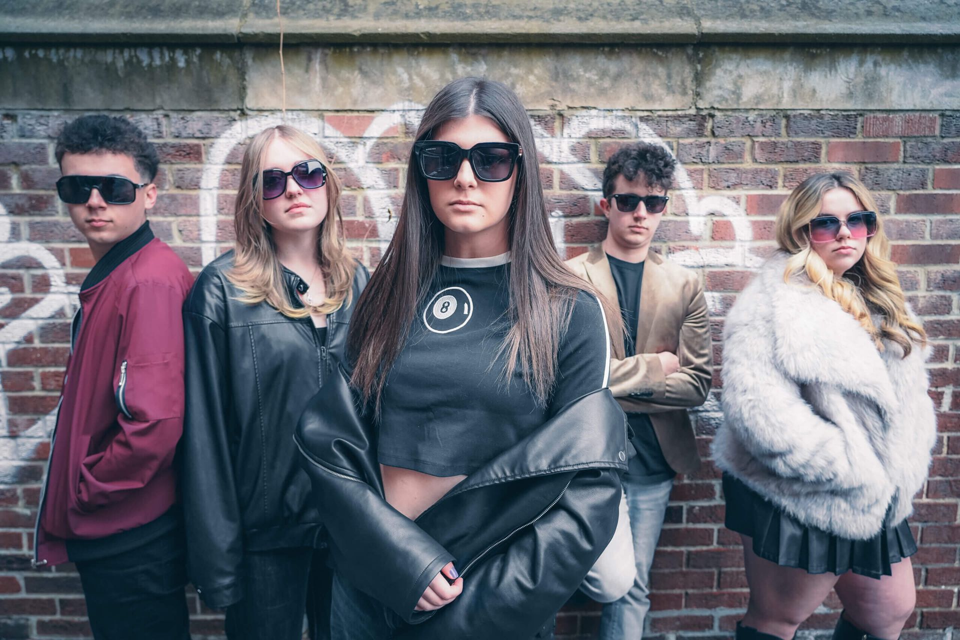 Five people in sunglasses and stylish coats posing in front of a brick wall outdoors. The Ultrasonik band.