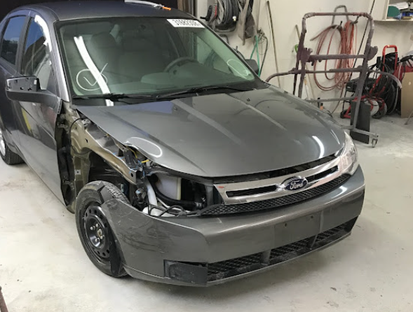 Damaged gray sedan with front-left body damage in an auto repair shop