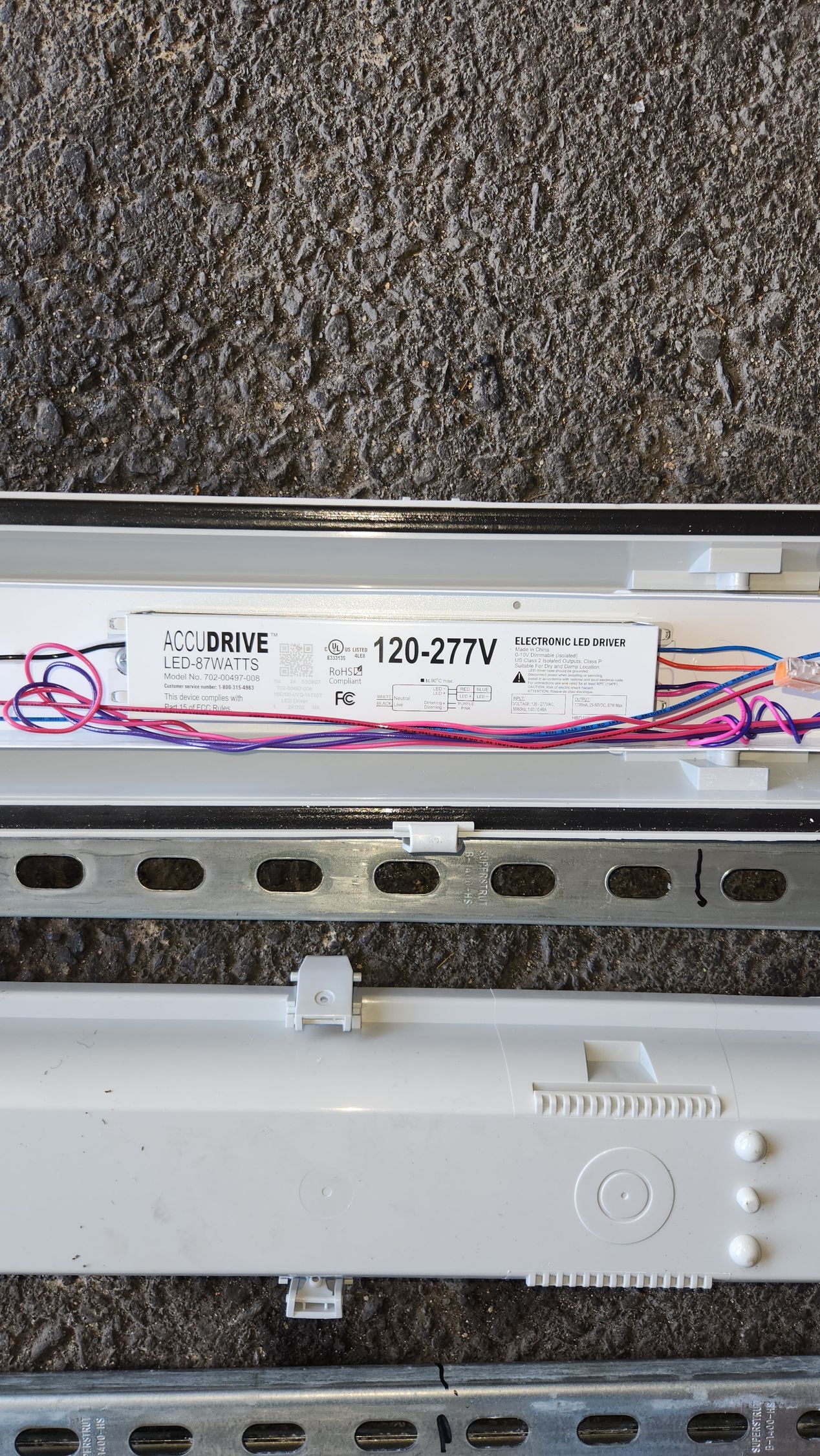 Fluorescent light fixture components: ballast with colored wires, metal bracket, and light housing, lying on carpet.
