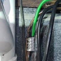 Close-up of electrical wires, including a green wire, secured with a wire connector against a dark background.