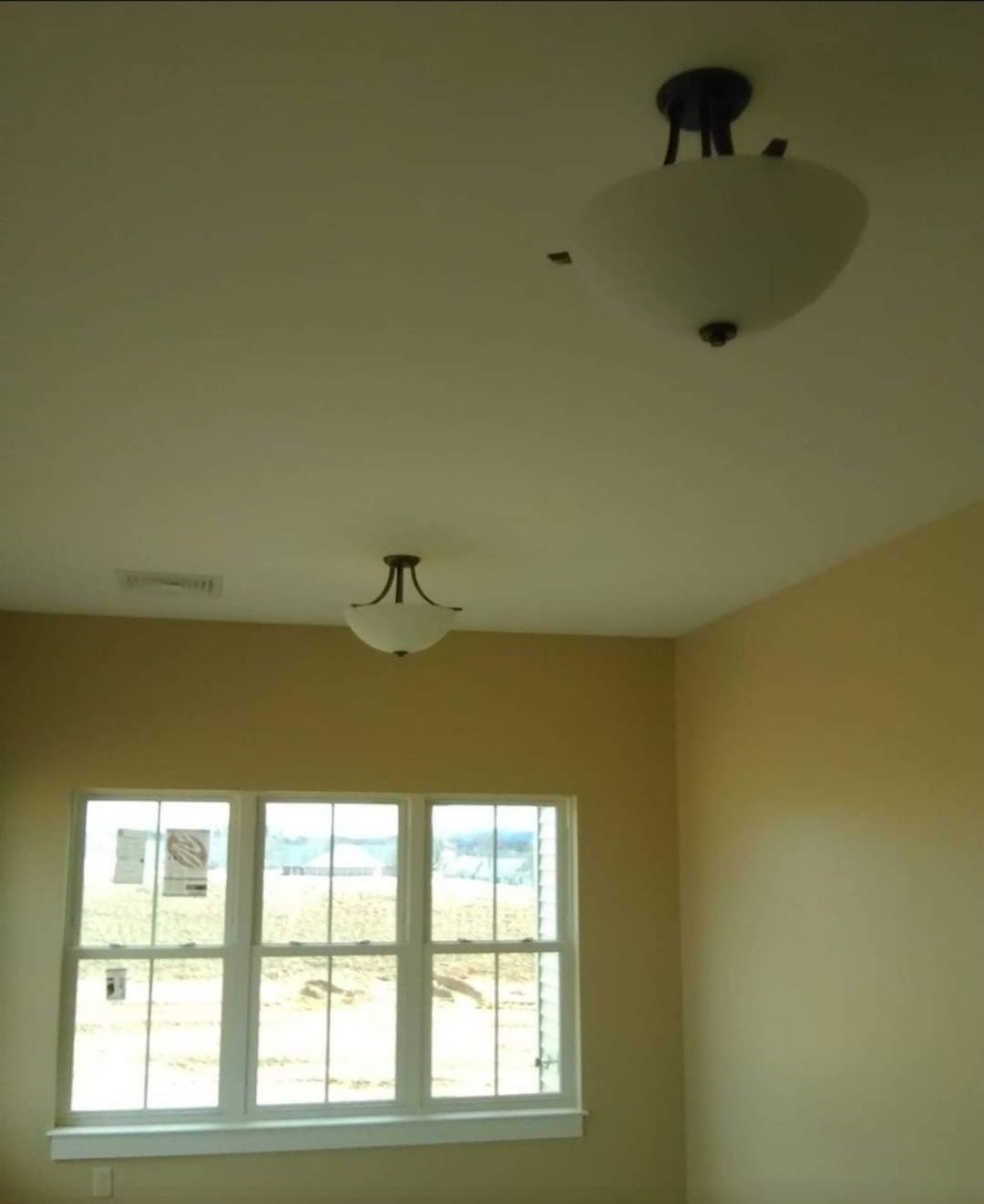 Two ceiling lights in a room with a window. The walls are light yellow.