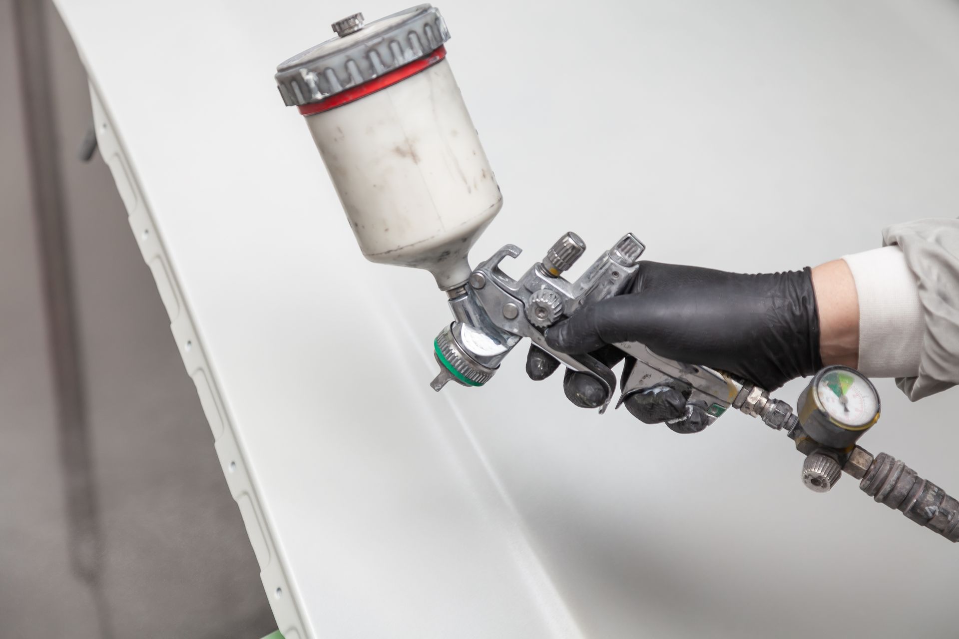 A person wearing black gloves uses a spray gun to apply paint to a smooth white surface.