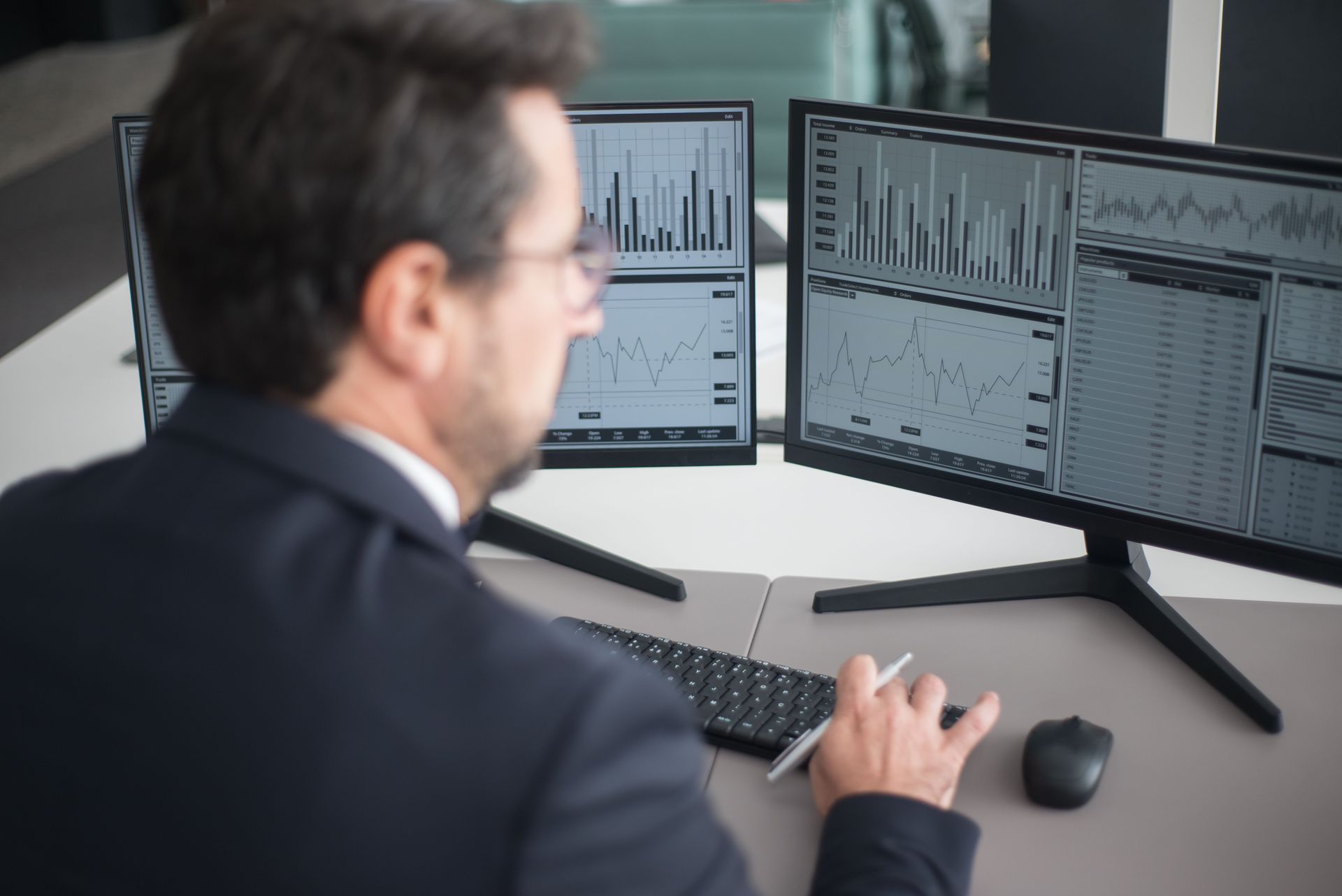 Person in a suit analyzing stock charts on dual computer monitors at a d.
