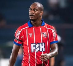 Um homem de camisa vermelha com listras finas azuis está jogando futebol