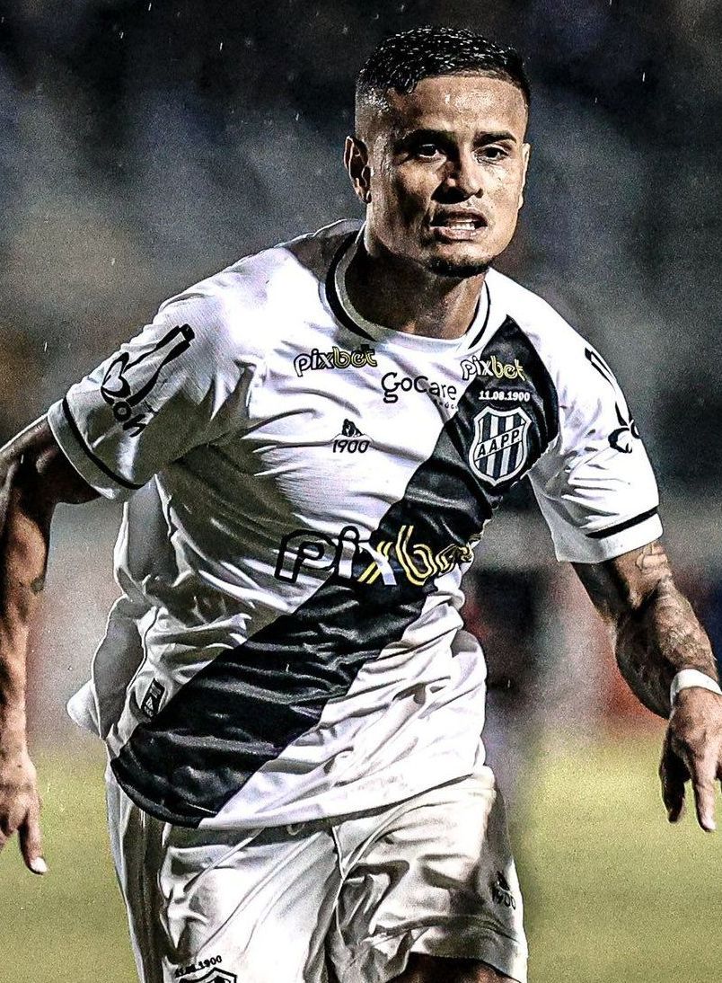 Um jogador de futebol com uniforme branco e preto está correndo em um campo.