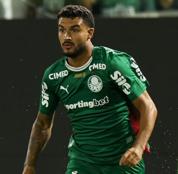 Jogador de camisa verde correndo num campo de futebol