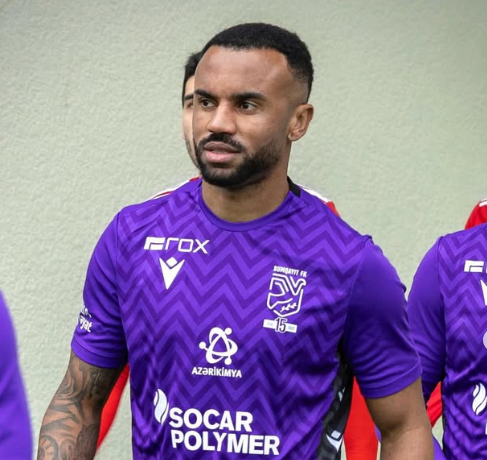 Um homem de camisa roxa está olhando para frente entrando em campo para um jogo de futebol.