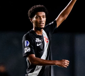 Um jovem com uma camisa de futebol branca e preta está correndo em um campo.